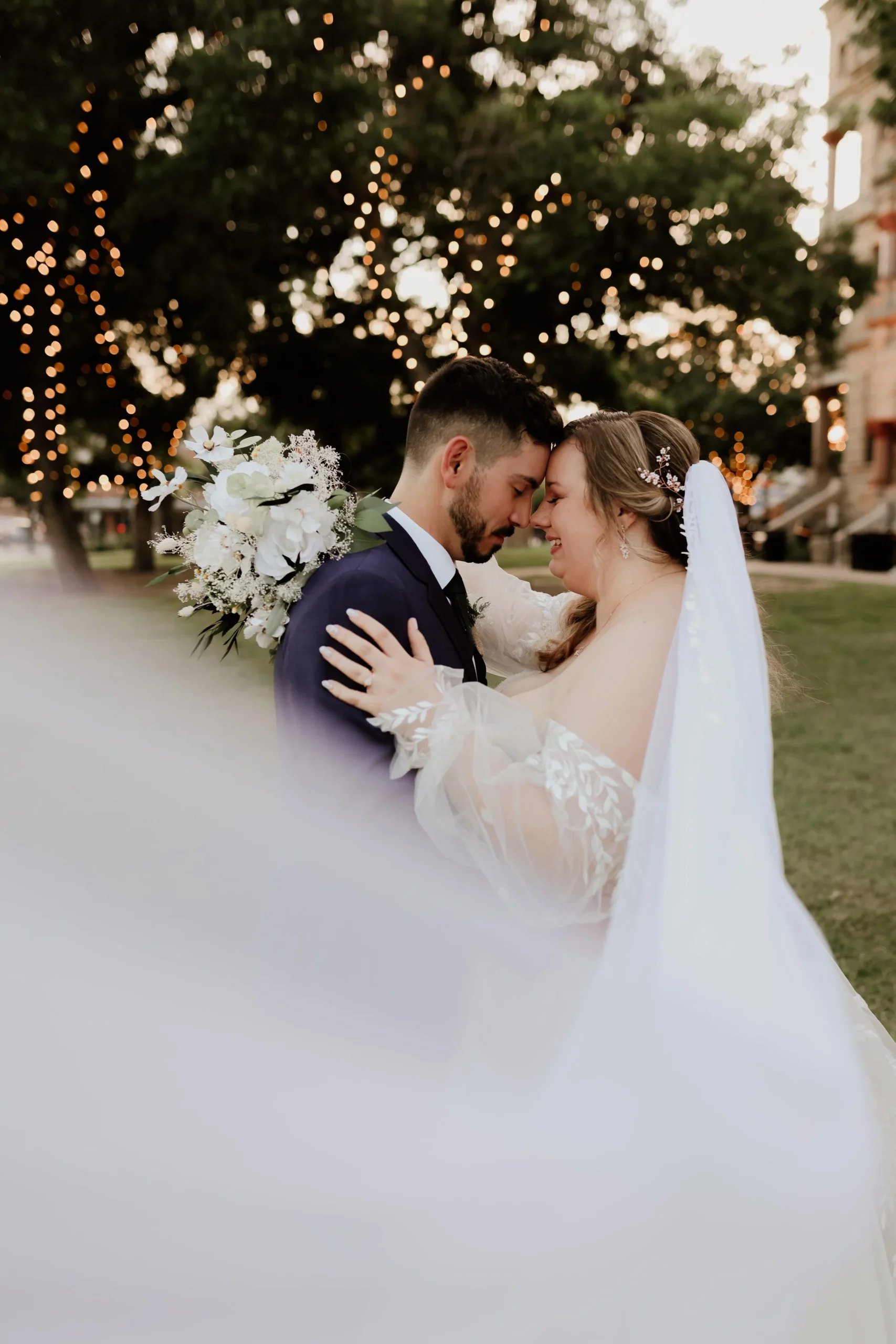 Bride and groom hugging, with the bride's veil stretched out to the lens for a whimsical, romantic look.