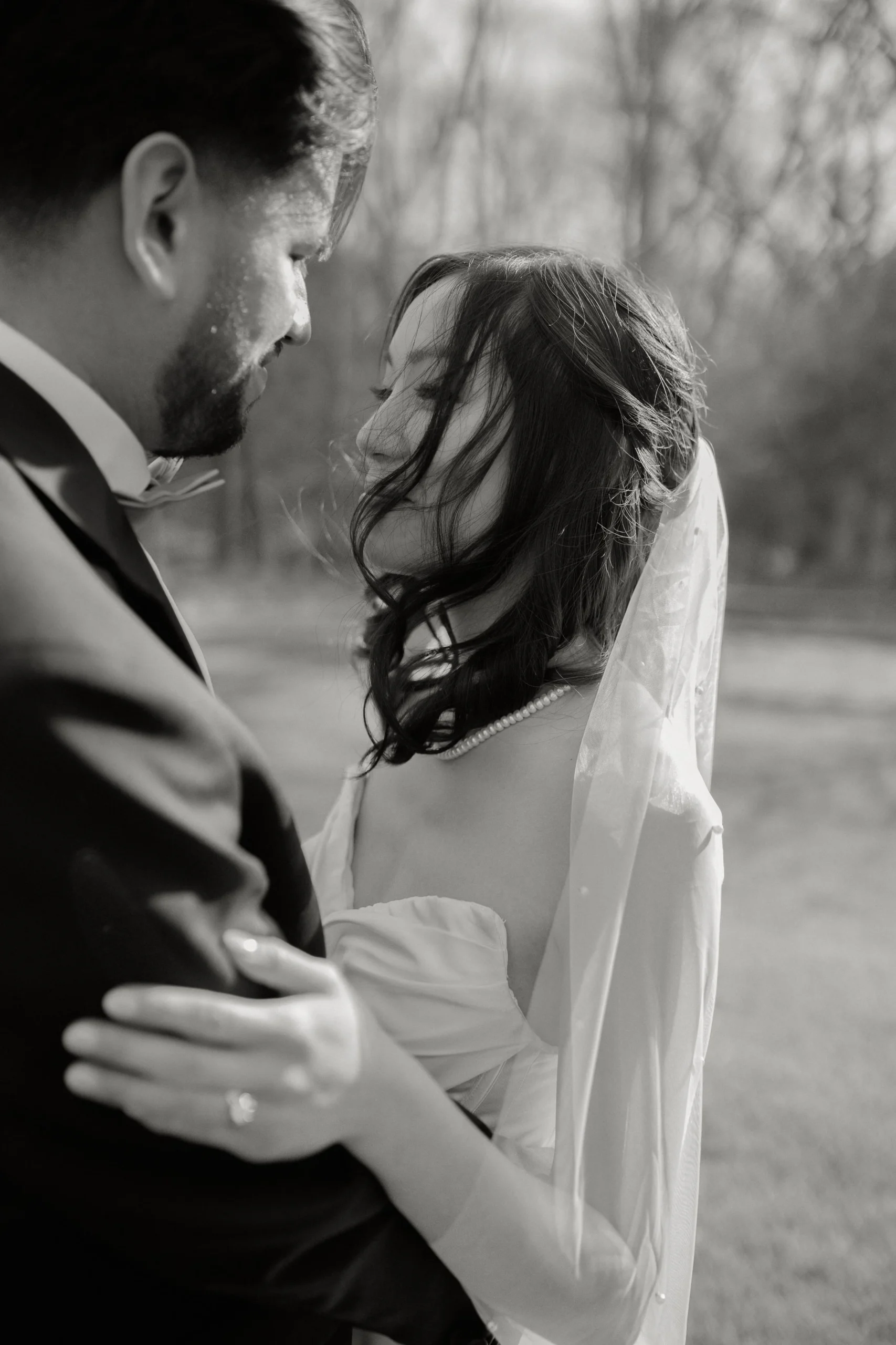 Black and white candid photo of a bride and groom, with windswept hair and a pearl veil.