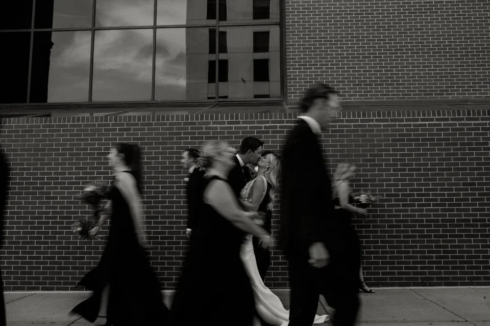 Bride and Groom kissing with their wedding party celebrating behind them