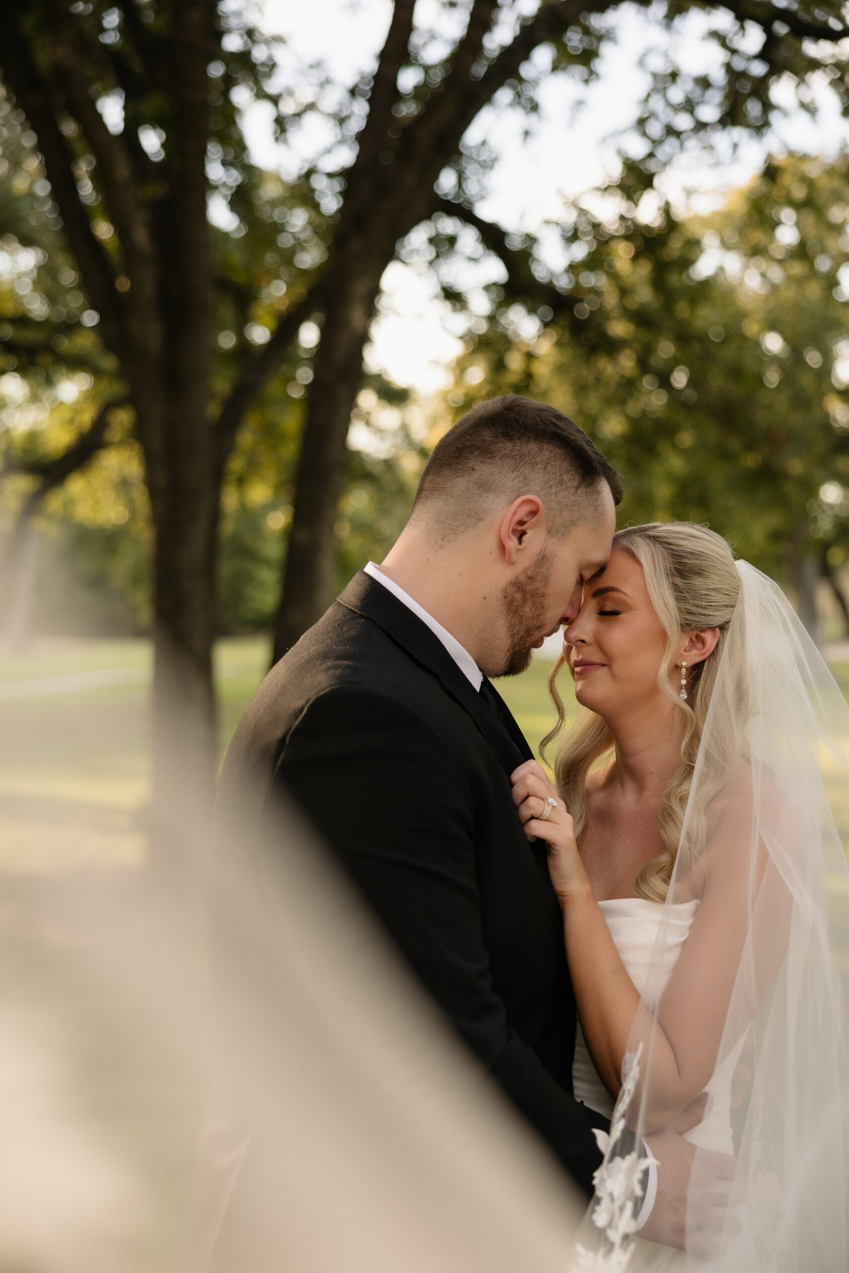 romantic photo of bride and groom in golden light with her wedding veil around them.