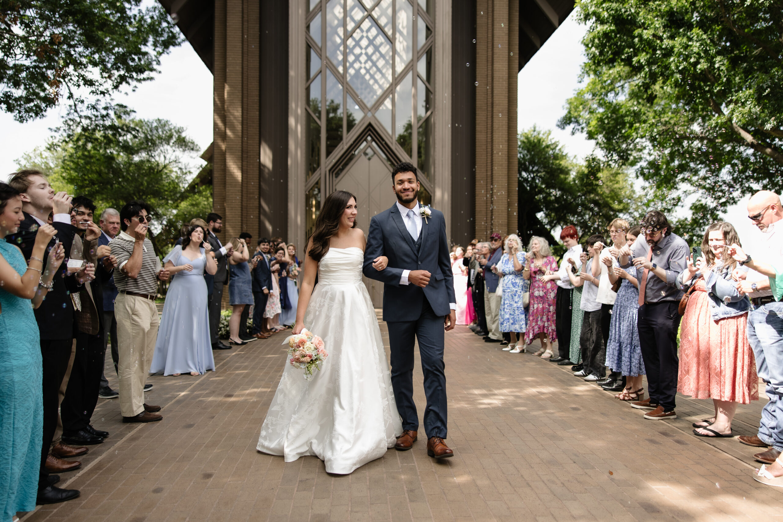 Newlywed couple leaving the Marty Leonard Chapel, with guests celebrating around them.